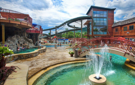 a spa/water park with large open pools, an enclosed building, a bridge, and a water slide in the background
