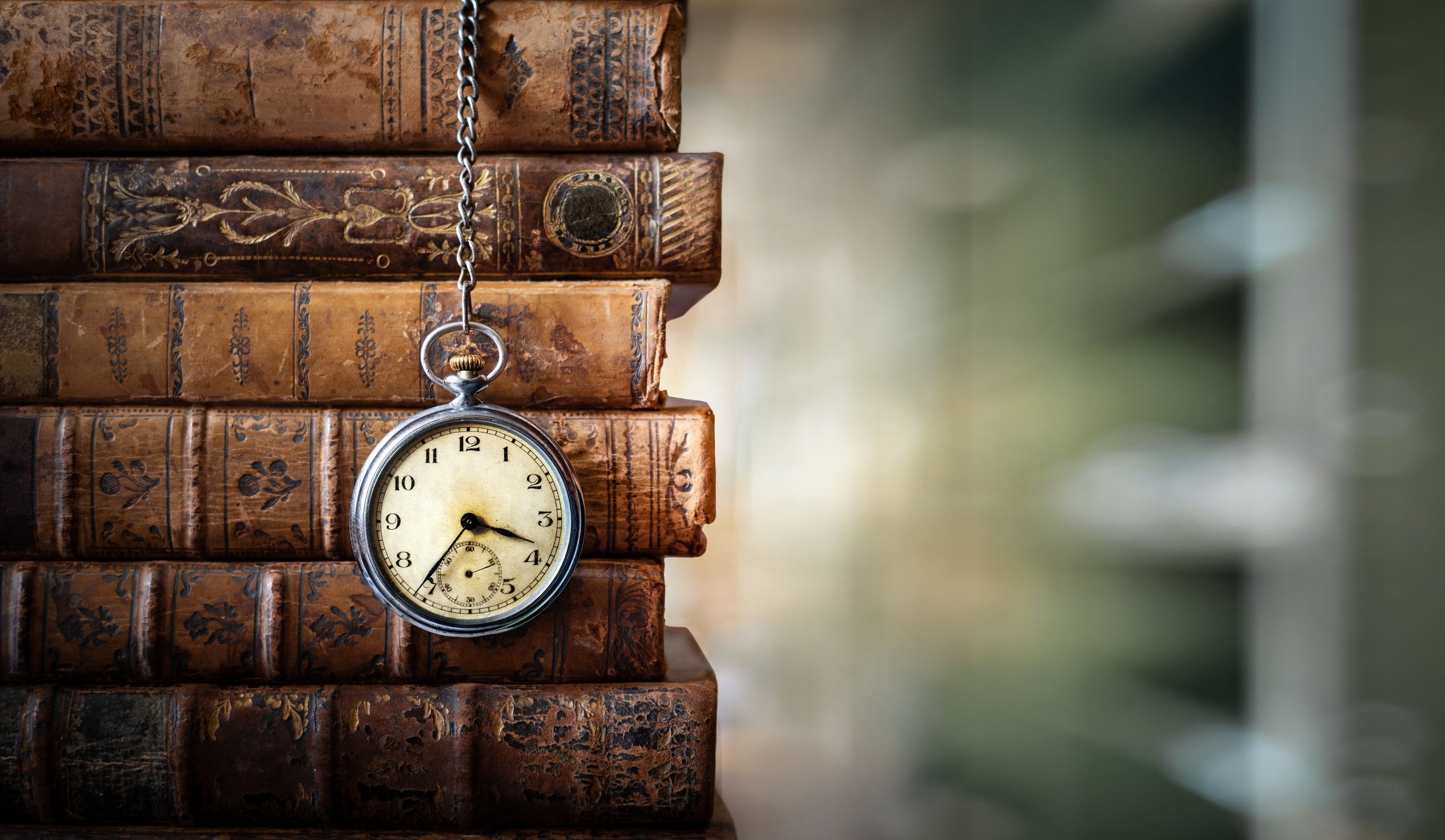 a stack of books with a pocketwatch hanging in front of the spines
